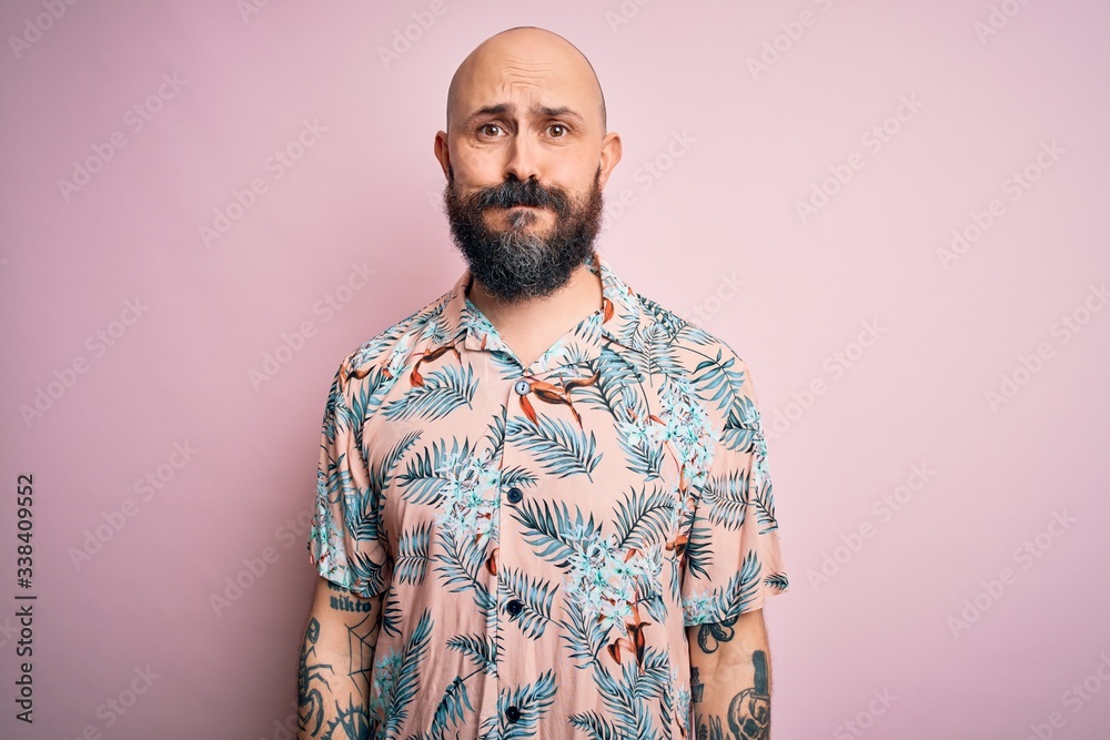 Handsome bald man with beard and tattoo wearing casual floral shirt over pink background puffing cheeks with funny face. Mouth inflated with air, crazy expression. Handsome bald man with beard and tattoo wearing casual floral shirt over pink background puffing cheeks with funny face. Mouth inflated with air, crazy expression.