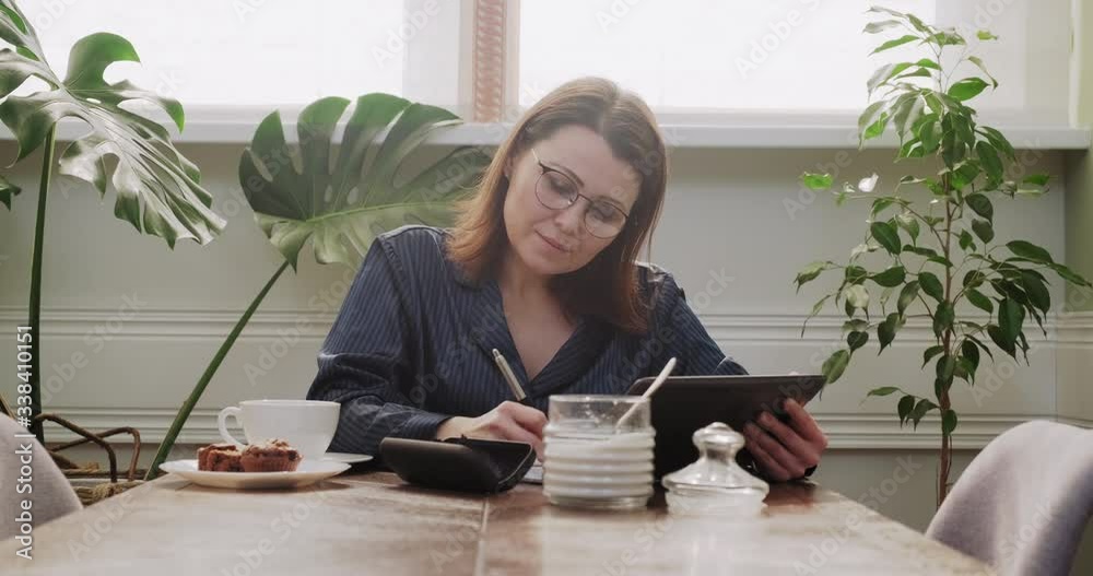 Female reading digital tablet, writing in business notebook, working remotely Female reading digital tablet, writing in business notebook, working remotely