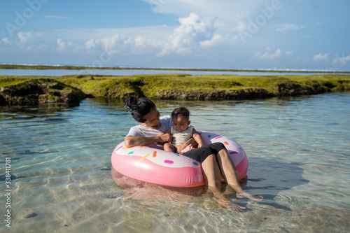 asian mother and baby ride the rubber ring float on the beach while enjoying a vacation at the beach