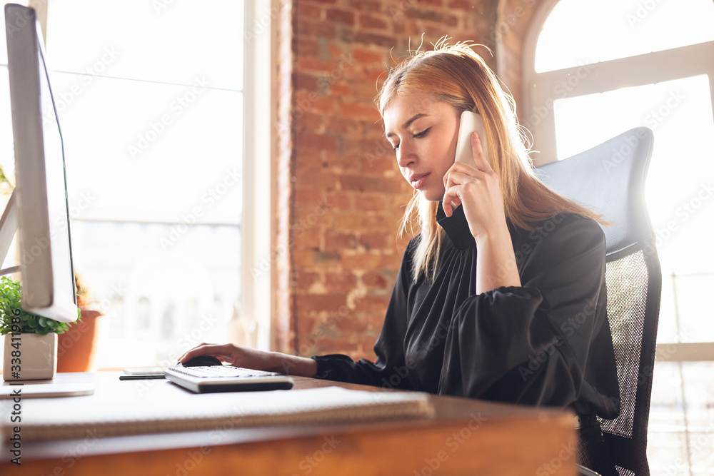 Talking on phone. Caucasian young woman in business attire working in office. Young businesswoman, manager doing tasks with smartphone, laptop, tablet has online conference. Finance, job. Talking on phone. Caucasian young woman in business attire working in office. Young businesswoman, manager doing tasks with smartphone, laptop, tablet has online conference. Finance, job.