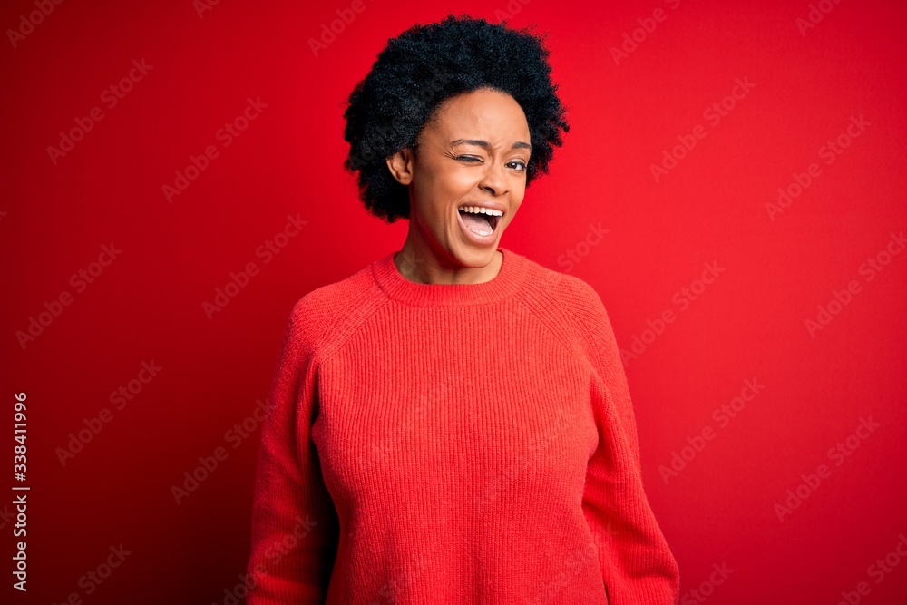 Young beautiful African American afro woman with curly hair wearing casual sweater winking looking at the camera with sexy expression, cheerful and happy face.
