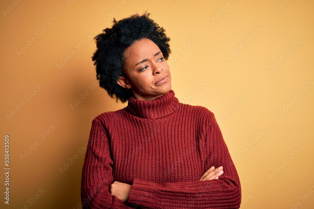 Young beautiful African American afro woman with curly hair wearing casual turtleneck sweater looking to the side with arms crossed convinced and confident