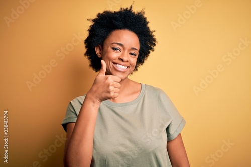 Young beautiful African American afro woman with curly hair wearing casual t-shirt doing happy thumbs up gesture with hand. Approving expression looking at the camera showing success. © Krakenimages.com