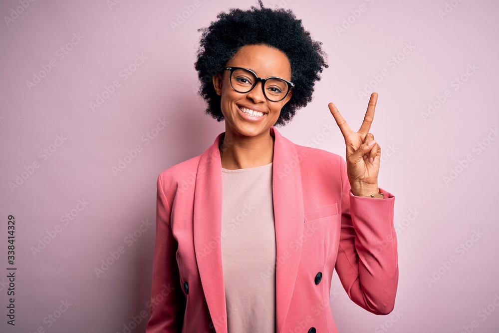 Young beautiful African American afro businesswoman with curly hair wearing pink jacket showing and pointing up with fingers number two while smiling confident and happy. Young beautiful African American afro businesswoman with curly hair wearing pink jacket showing and pointing up with fingers number two while smiling confident and happy.