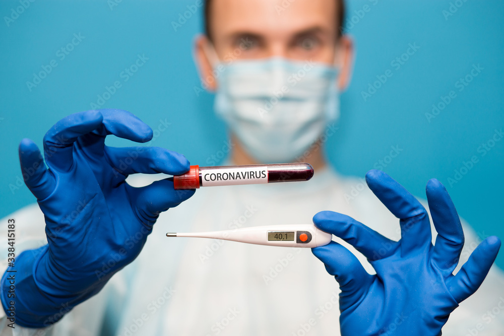 Doctor in protective mask and gloves holds medical thermometer set 40 and test tube containing blood tested for coronavirus. Laboratory testing patients blood for presence of coronavirus COVID-19. Doctor in protective mask and gloves holds medical thermometer set 40 and test tube containing blood tested for coronavirus. Laboratory testing patients blood for presence of coronavirus COVID-19.