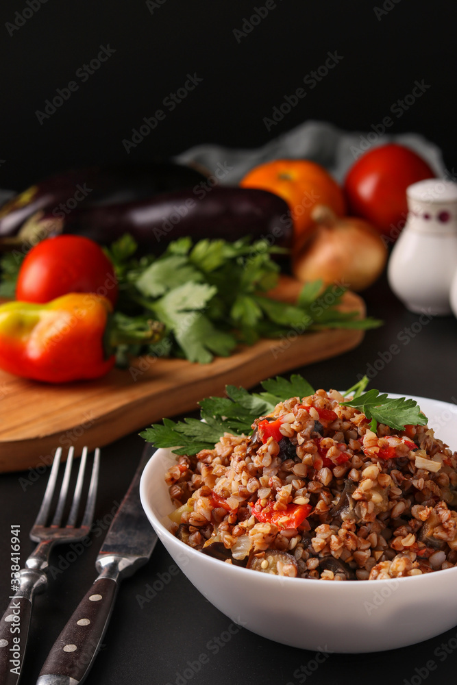 Healthy buckwheat cooked with vegetables in a white bowl on a dark background, Vertical orientation, Closeup