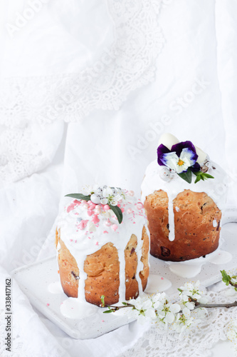 Easter Orthodox sweet bread, two Easter cakes decorated with flowers and sweets on a white marble plate on a white wooden background. Holidays breakfast concept with copy space.