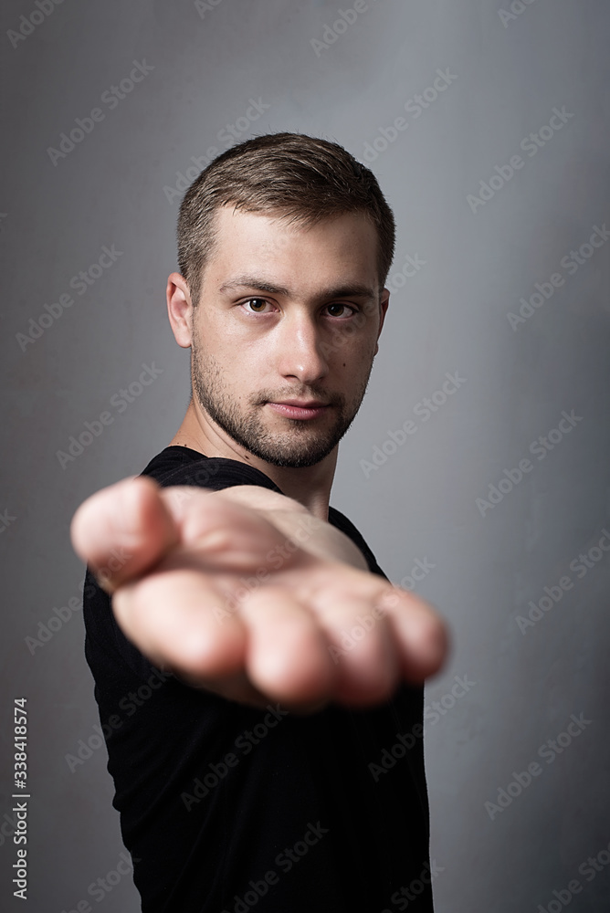 Portrait of young successful serious man extends a hand on a grey background. men in black t-shirt holding copy space on palm.