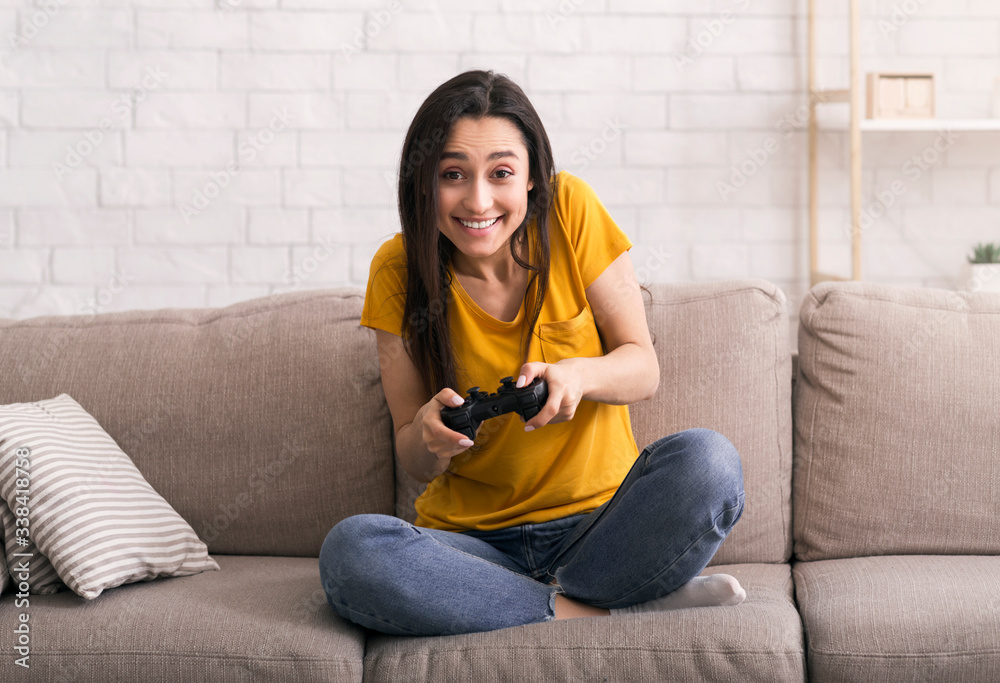 Quarantine pastimes. Joyful Latin girl with joystick playing video games on sofa at home Quarantine pastimes. Joyful Latin girl with joystick playing video games on sofa at home