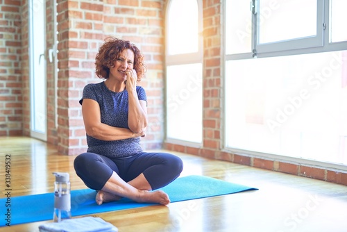 Middle age beautiful sportswoman wearing sportswear sitting on mat practicing yoga at home looking stressed and nervous with hands on mouth biting nails. Anxiety problem.