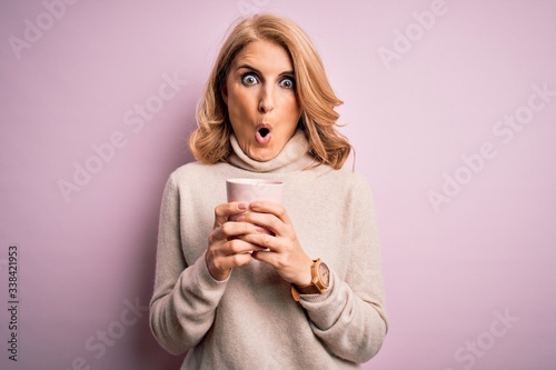 Middle age beautiful blonde woman drinking pink mug of coffee over isolated background scared in shock with a surprise face, afraid and excited with fear expression