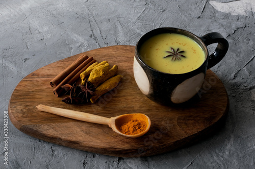 Cup of turmeric golden milk served with spices –cinnamon and star anise on grey concrete background.