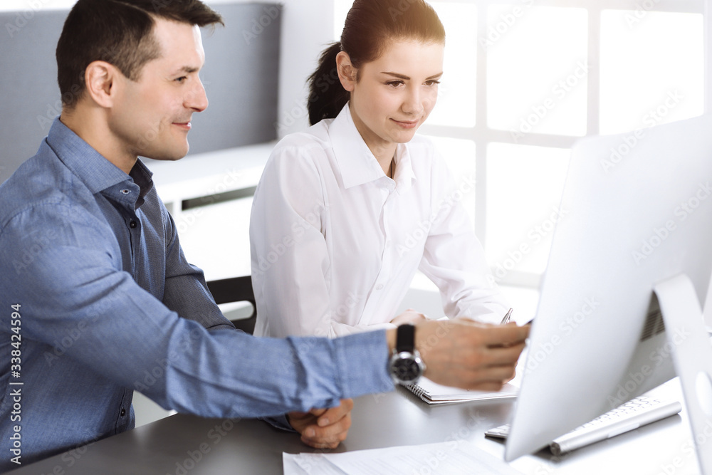 Friendly smiling businessman and woman working with computer in modern office. Headshot at meeting or workplace. Teamwork, partnership and business concept Friendly smiling businessman and woman working with computer in modern office. Headshot at meeting or workplace. Teamwork, partnership and business concept