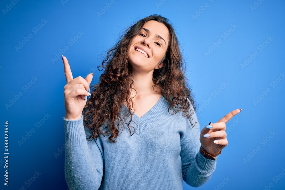 Young beautiful woman with curly hair wearing blue casual sweater over isolated background smiling confident pointing with fingers to different directions. Copy space for advertisement Young beautiful woman with curly hair wearing blue casual sweater over isolated background smiling confident pointing with fingers to different directions. Copy space for advertisement