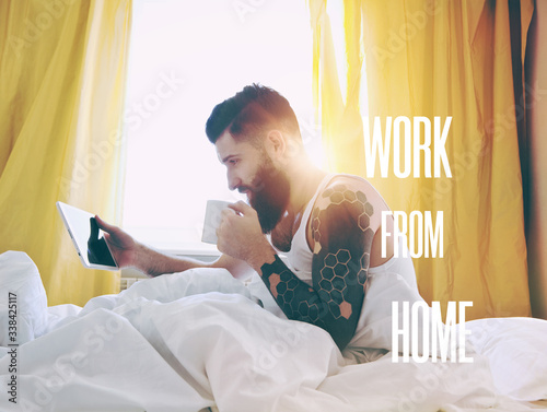 Bearded man lying in bed with morning coffee and digital tablet photo