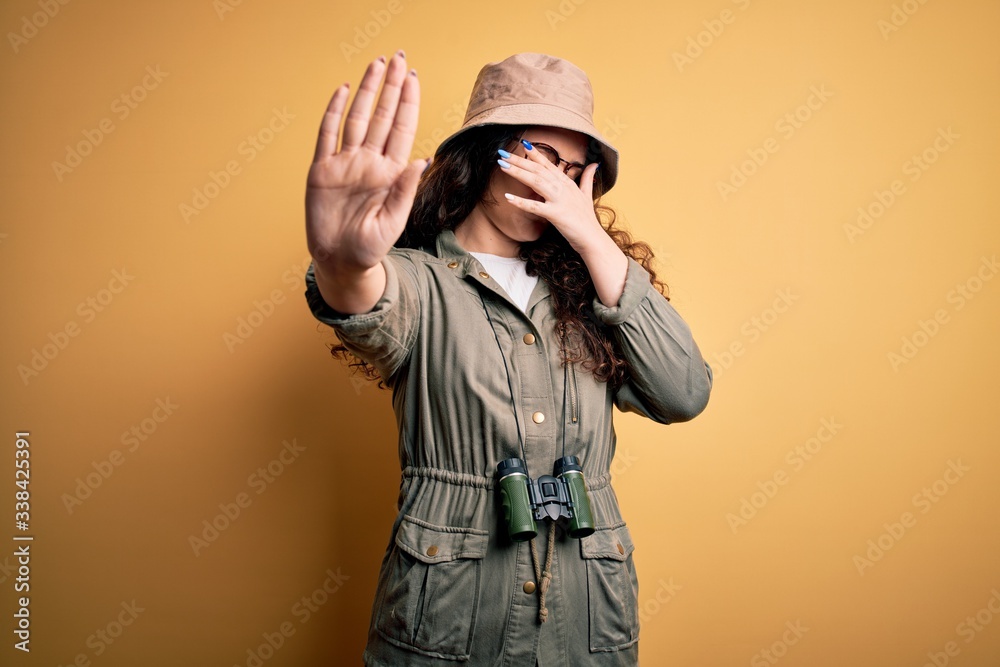 Young beautiful tourist woman on vacation wearing explorer hat and binoculars covering eyes with hands and doing stop gesture with sad and fear expression. Embarrassed and negative concept. Young beautiful tourist woman on vacation wearing explorer hat and binoculars covering eyes with hands and doing stop gesture with sad and fear expression. Embarrassed and negative concept.