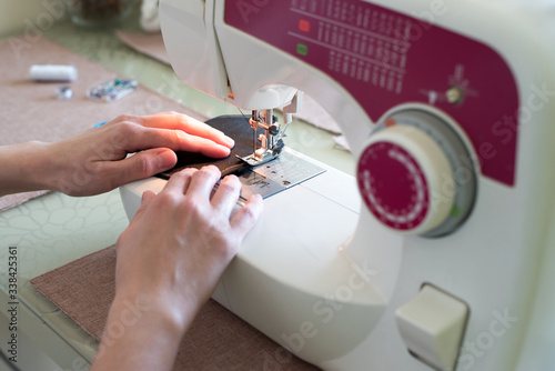 Close-up woman hands using sewing machine to sew black cotton face medical mask. DIY or individual protect on quarantine concept. Soft focus