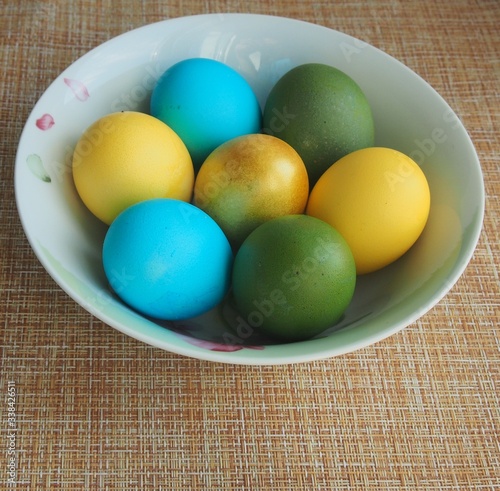 Colorful Easter eggs lie in a white porcelain plate. Blue, green, yellow, Golden eggs.