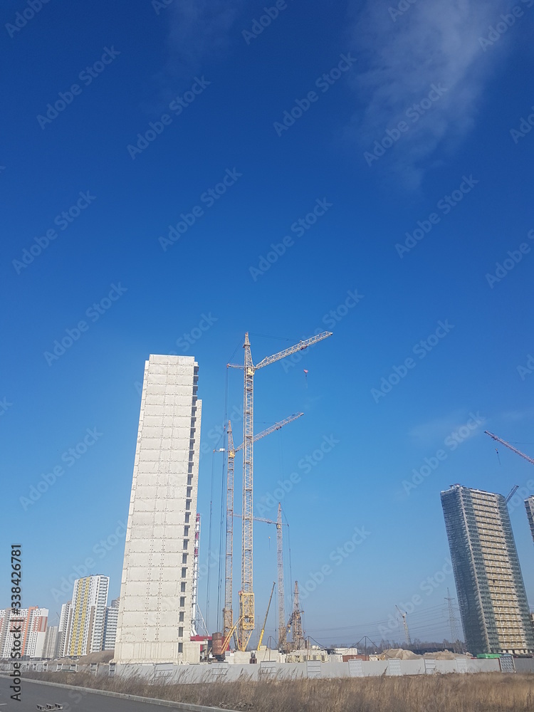 construction of a new residential building against a clear blue sky. next to the house are high construction cranes