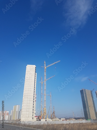 construction of a new residential building against a clear blue sky. next to the house are high construction cranes