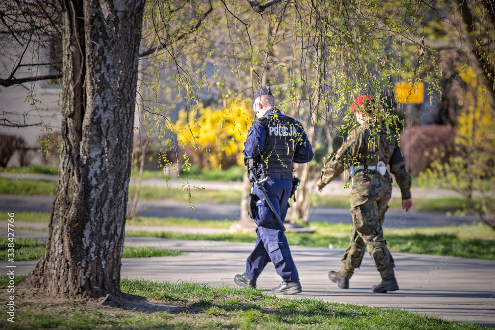Policjant i żołnierz patrolują park w czasie epidemii.  - obrazy, fototapety, plakaty 