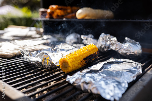 Corn, burger patties, meat and baguettes on a Grill with aluminium foil