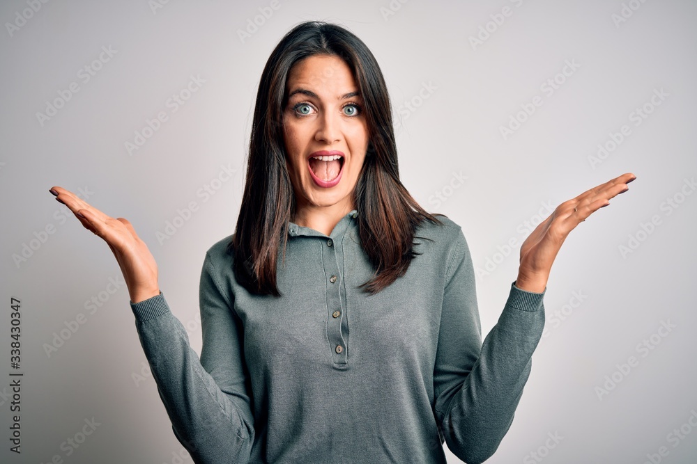 Young brunette woman with blue eyes wearing casual green sweater over white background celebrating crazy and amazed for success with arms raised and open eyes screaming excited. Winner concept Young brunette woman with blue eyes wearing casual green sweater over white background celebrating crazy and amazed for success with arms raised and open eyes screaming excited. Winner concept