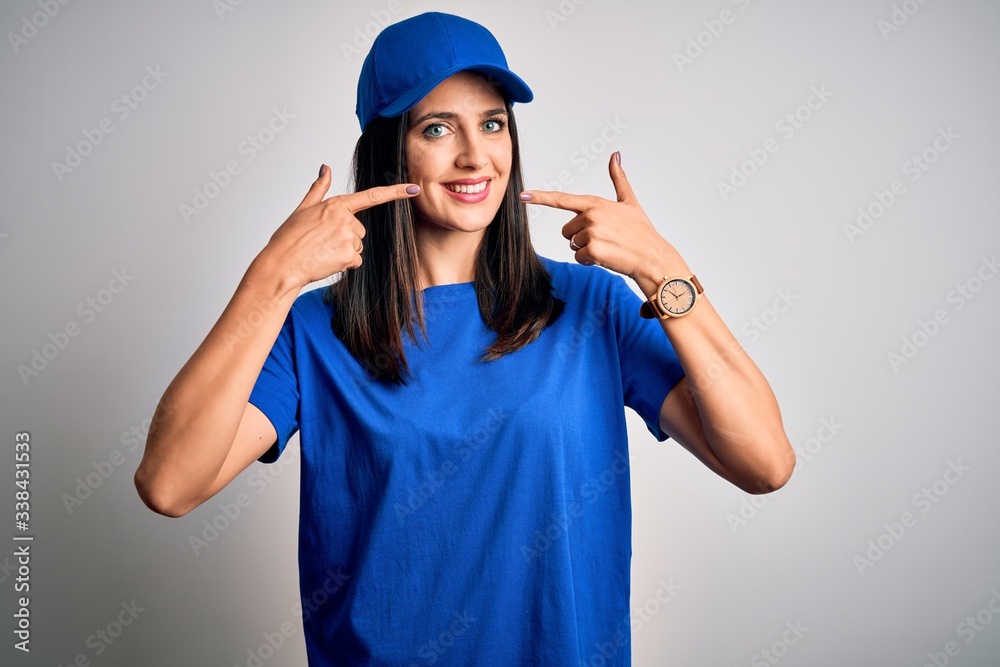 Young delivery woman with blue eyes wearing cap standing over blue background smiling cheerful showing and pointing with fingers teeth and mouth. Dental health concept. Young delivery woman with blue eyes wearing cap standing over blue background smiling cheerful showing and pointing with fingers teeth and mouth. Dental health concept.