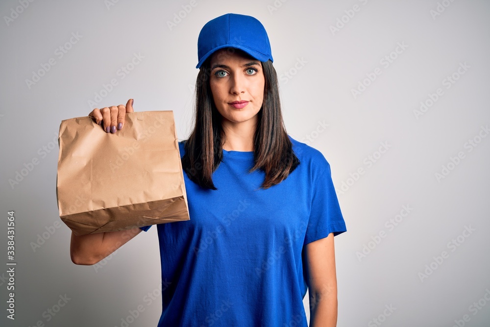 Young delivery woman with blue eyes wearing cap holding paper bag with food with a confident expression on smart face thinking serious Young delivery woman with blue eyes wearing cap holding paper bag with food with a confident expression on smart face thinking serious