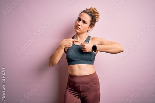 Young beautiful blonde sportswoman doing sport wearing sportswear over pink background In hurry pointing to watch time, impatience, looking at the camera with relaxed expression © Krakenimages.com