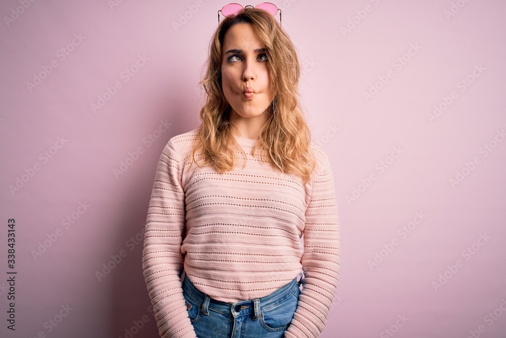 Young beautiful blonde woman wearing casual sweater and sunglasses over pink background making fish face with lips, crazy and comical gesture. Funny expression. Young beautiful blonde woman wearing casual sweater and sunglasses over pink background making fish face with lips, crazy and comical gesture. Funny expression.