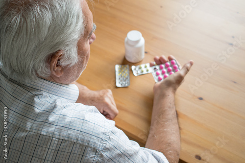 sick senior man sit next to table at home look at pills sad alone