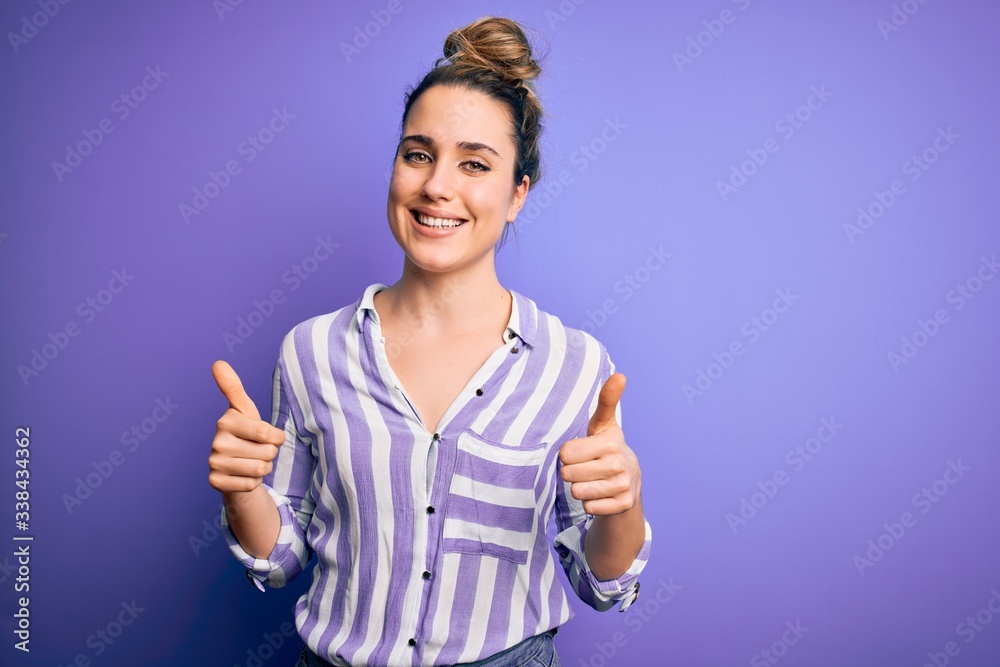 Young beautiful blonde woman wearing casual striped shirt standing over purple background success sign doing positive gesture with hand, thumbs up smiling and happy. Cheerful expression and winner Young beautiful blonde woman wearing casual striped shirt standing over purple background success sign doing positive gesture with hand, thumbs up smiling and happy. Cheerful expression and winner