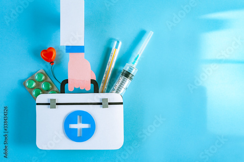 Doctor hand hold first aid kit with thermometer and syringe on blue background. World Health Day. Healthcare concept. Space for text. Soft focus. Top view.