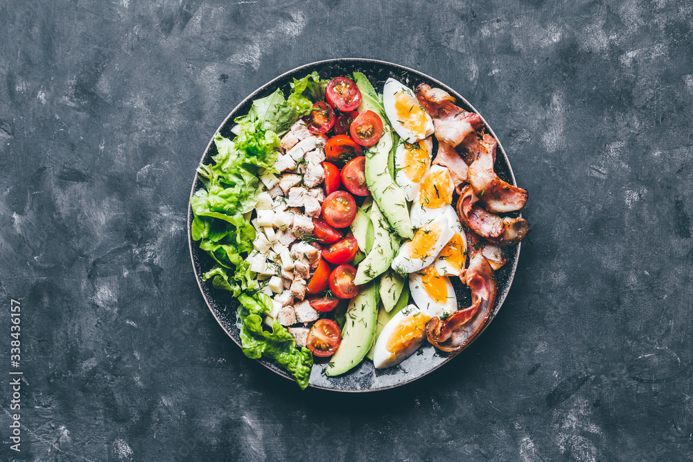 Cobb salad with chicken, avocado, tomatoes, eggs, bacon and cheese with sauce on a black  table top view