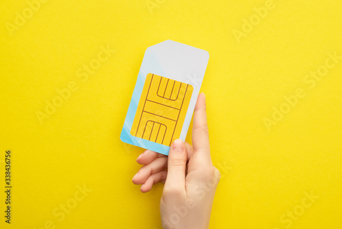 Foto cropped view of woman holding sim card on yellow background