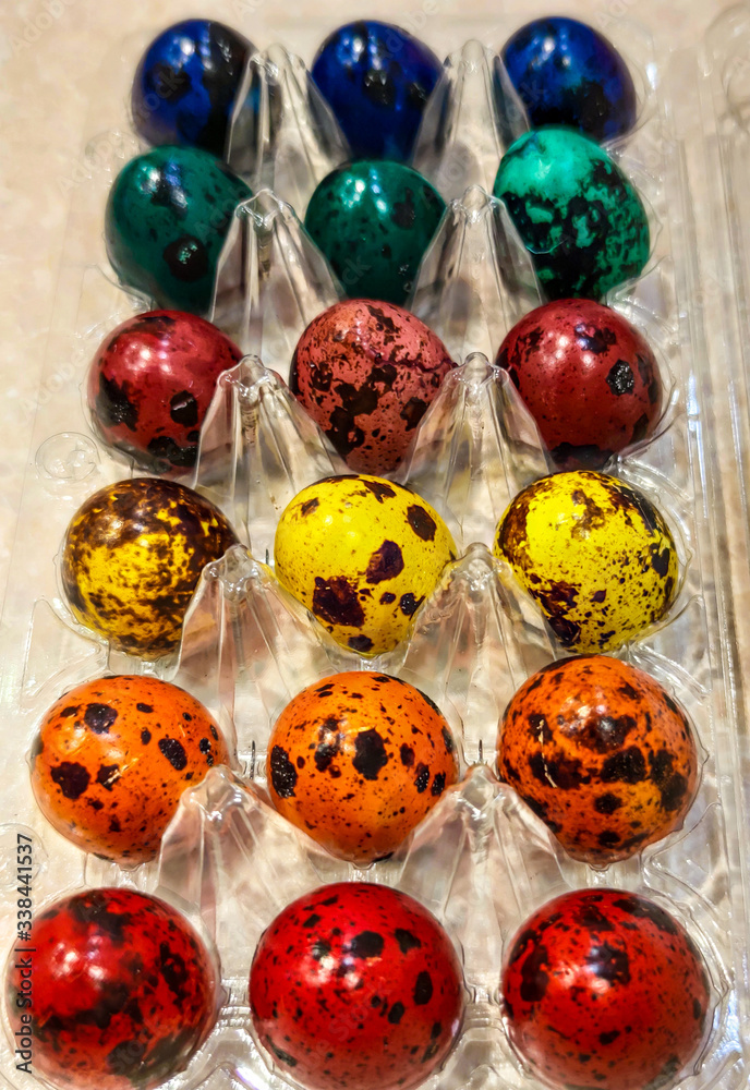 Religious Easter holiday, packaging with spotted quail eggs painted in different colors, colorful rows, red, orange and other colors.