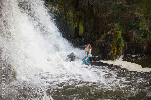 beautiful red-haired girl bathes in a stormy stream of a waterfall, hot summer © AKaltykova
