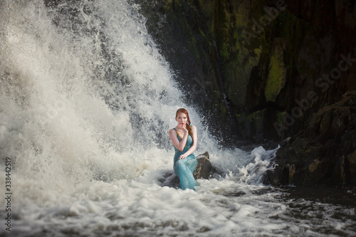 beautiful red-haired girl bathes in a stormy stream of a waterfall  hot summer