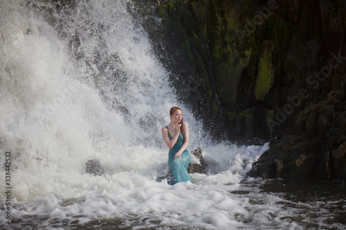 beautiful red-haired girl bathes in a stormy stream of a waterfall  hot summer