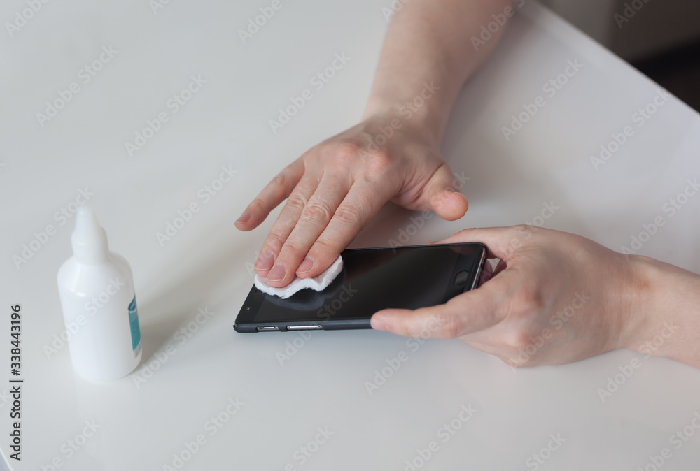 Man disinfects and wipes his smartphone with cotton pad. Cleaning cell phone with antiseptic close up Man disinfects and wipes his smartphone with cotton pad. Cleaning cell phone with antiseptic close up