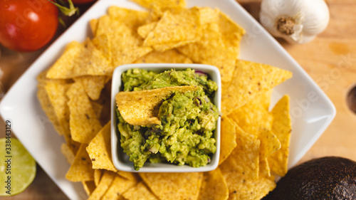 Corn Chips decorated in a Plate with Bowl full of Guacamole surrounded by Tomato , lemon, garlic and avocado