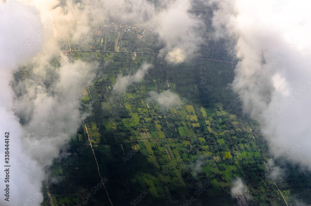 Fototapeta premium Aerial view of green fields looking through the clouds