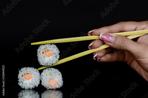 Sushi roll with salmon fish, rice, and white cheese. A hand holding chopsticks with one piece.