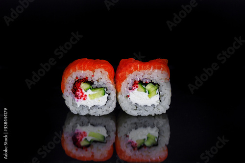 Tradishional Japanese sushi with red salmon, caviar, cucamber and cheese on black glass surface with reflection. Asian food concept.