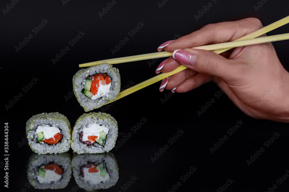 Sushi roll with salmon fish, cucamber, and white cheese. A hand holding chopsticks with one piece. Sushi roll with salmon fish, cucamber, and white cheese. A hand holding chopsticks with one piece.