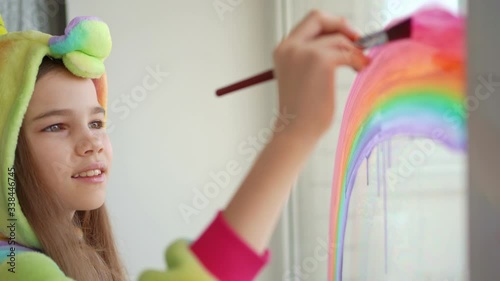teen girl in kigurumi draws rainbow on window. photo