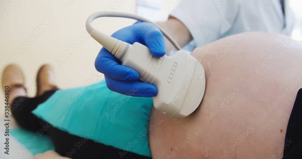 Ultrasound examination in doctors office. Close up shot on the ultrasound transducer on mothers belly Ultrasound examination in doctors office. Close up shot on the ultrasound transducer on mothers belly