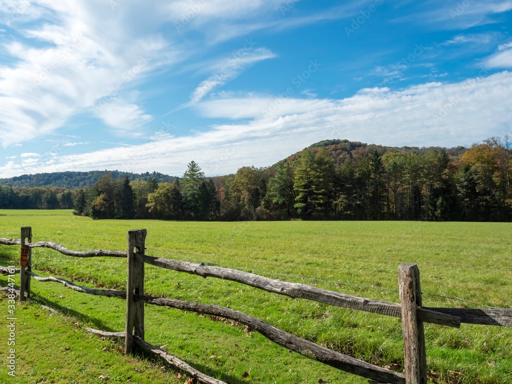 Landscape nature scene in the Laurel Highlands of Pennsylvania with a fence in the foreground and a meadow and tree line in the background with bright blue cloudy skies!
