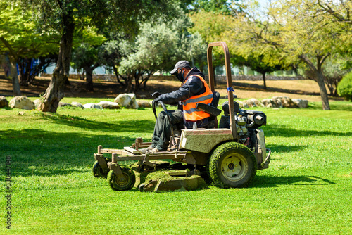 Man wearing black face mask mows the grass with lawn mower. Mow the lawns. photo